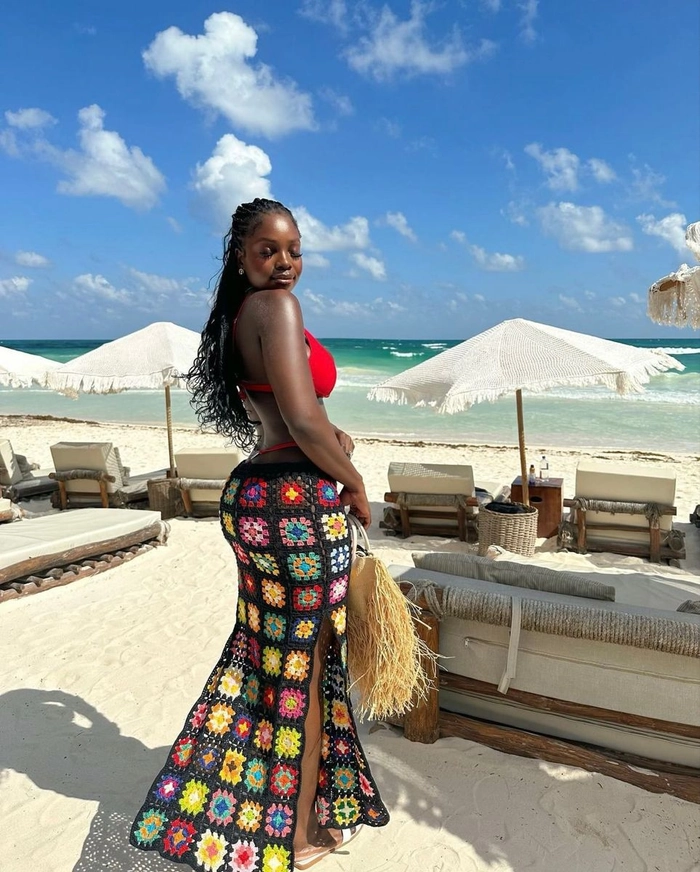 Woman with a voluminous afro hairstyle smiling at the beach in a colorful vacation outfit