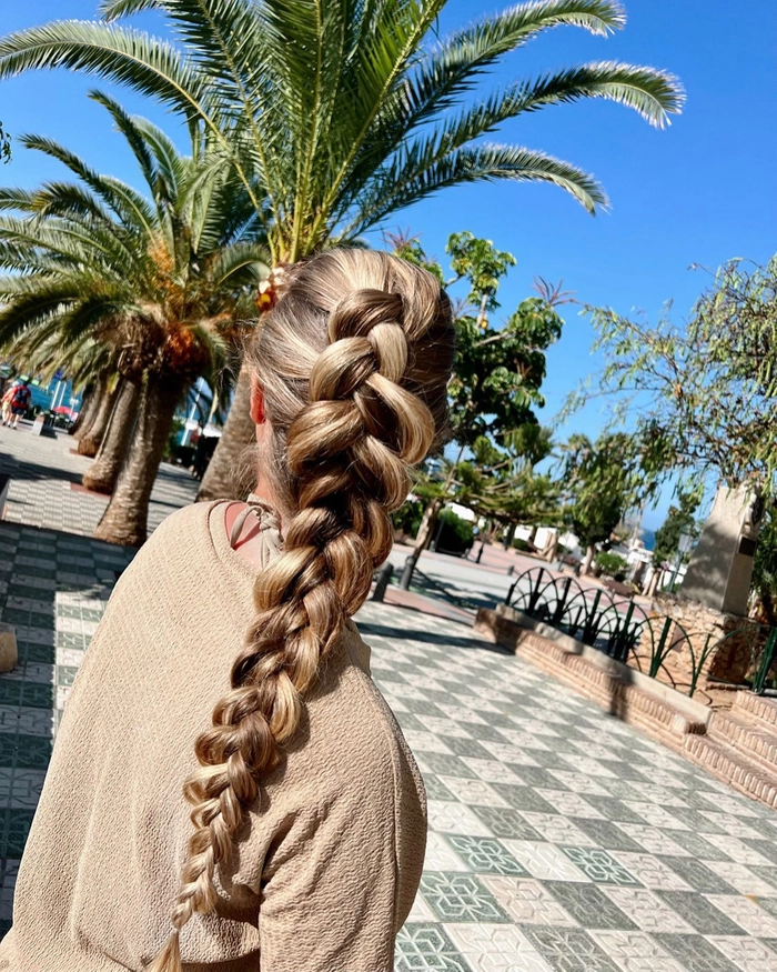 Woman with beach french braid hairstyle, waves and sand in background, bohemian aesthetic