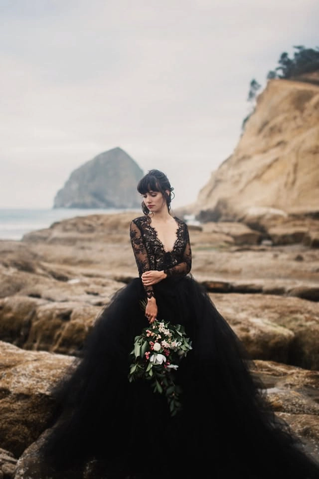 Coastal Elopement Hair Inspiration – Loose Curls with Delicate Floral Accent Bride with flowing beach waves and a small white flower in her hair, standing on the sand at sunset