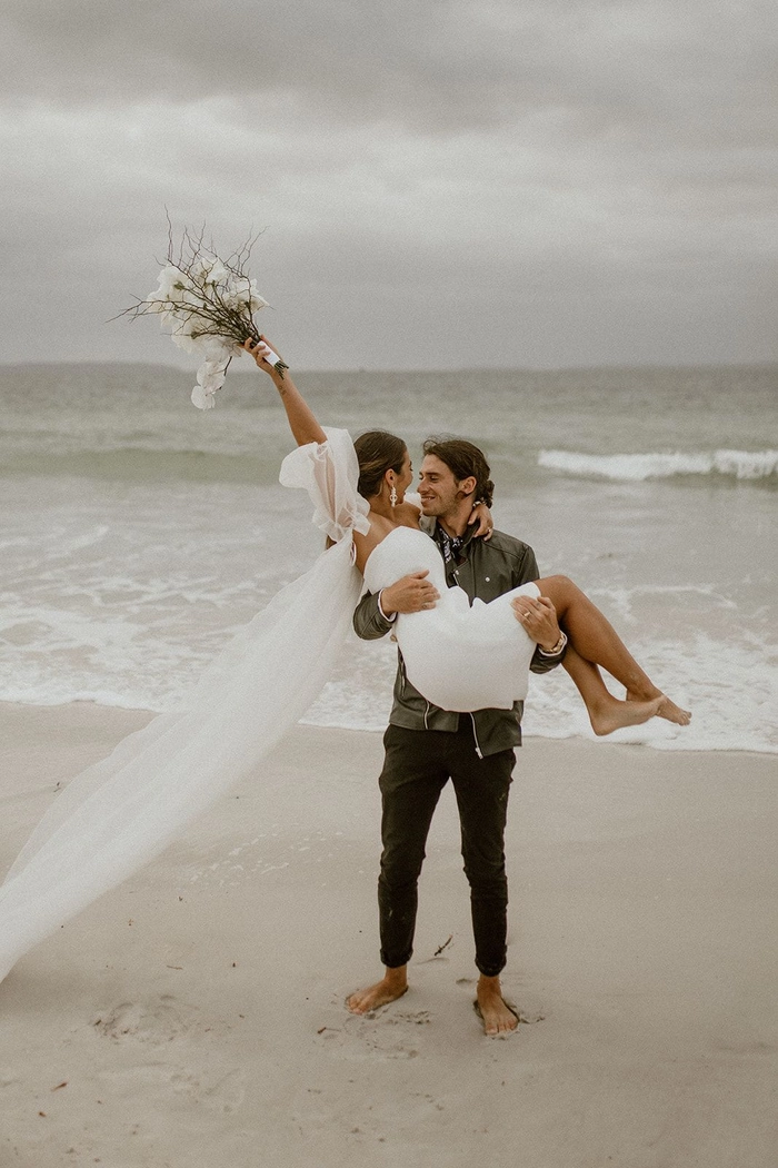 Coastal elopement hair inspiration featuring soft windswept waves and natural texture Bride with loose beach waves and a floral crown at a seaside elopement ceremony.