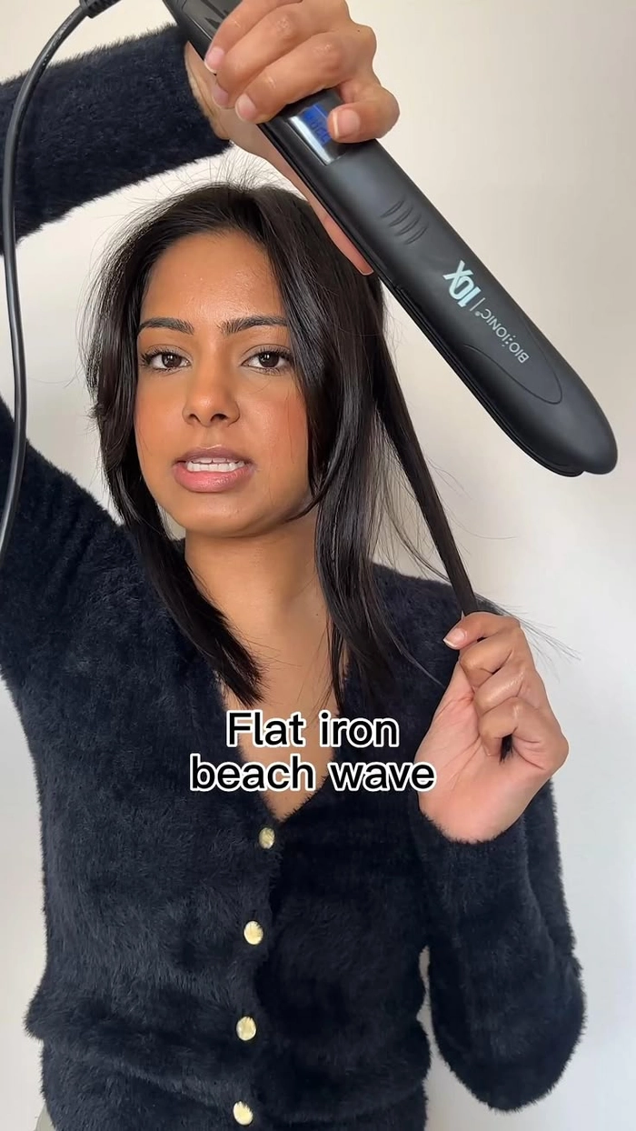 Woman using a flat iron to style her hair into loose beach waves