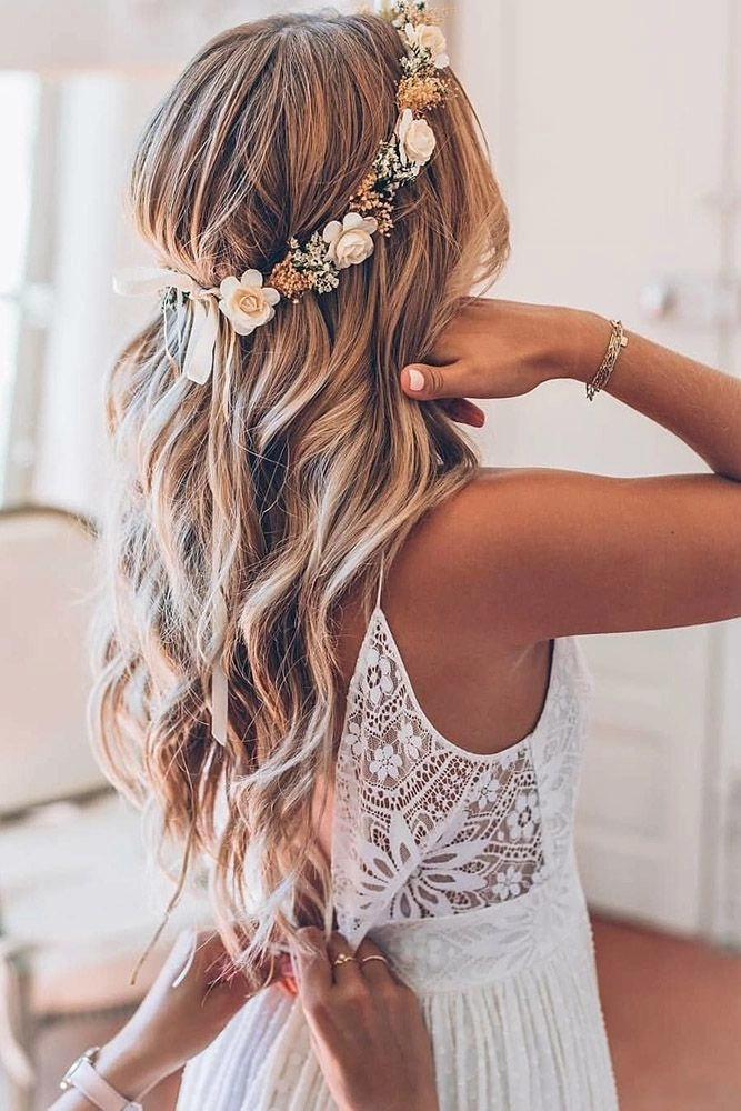 A woman wearing a floral crown in her beach-styled hair, smiling with ocean waves in the background