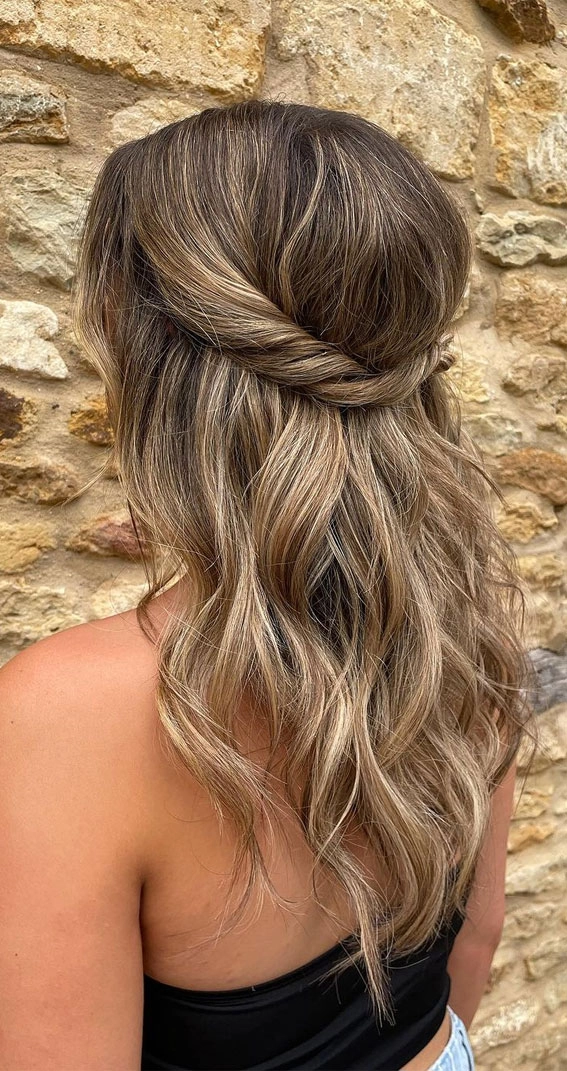 Half Up Half Down Beach Hair Style with Braid and Waves for a Casual Seaside Look A woman with half up half down beach hair styled with loose waves and a small braid, standing on the sandy shore
