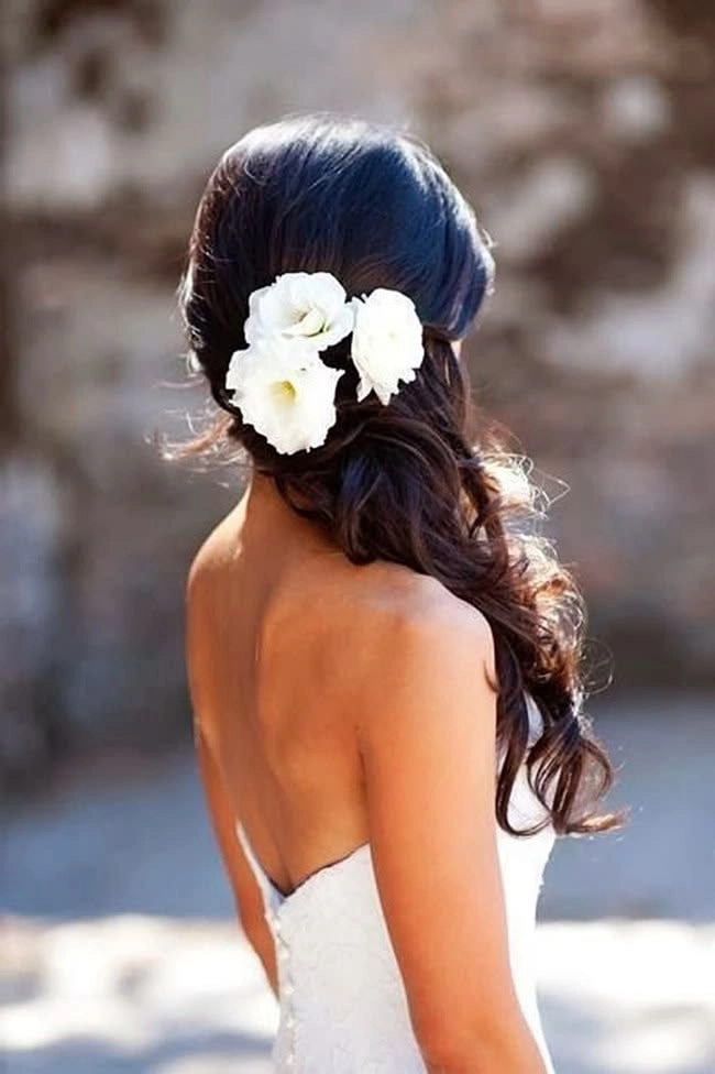 Short beach wedding hairstyle for a bride with tousled waves and a fresh flower accent