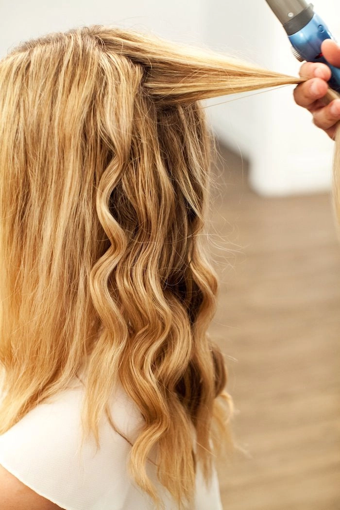 Woman with straight hair using a curling wand to create soft beach waves, styling tutorial step