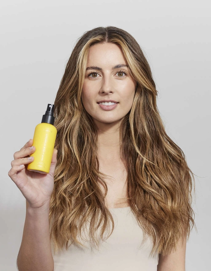 Top-rated UV protection hair sprays for healthy beach hairstyles at the shore Woman spritzing UV protection hair spray onto her beach waves under bright sun