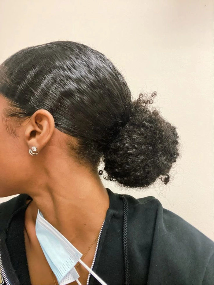 A woman with curly hair styled in a sleek, slicked back bun, showcasing an easy casual look