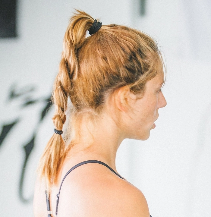 Casual ponytail variations for gym workouts - high ponytail with a side braid A woman tying a high ponytail before a gym workout, showing a practical casual hairstyle variation