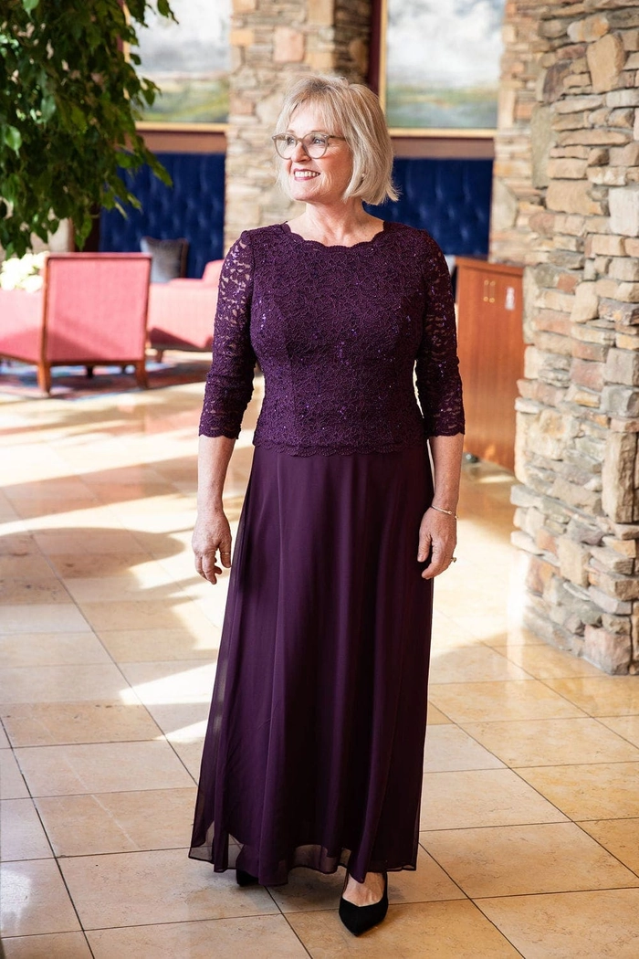 Elegant date night updo for mature women with soft waves and subtle highlights. A mature woman with elegant silver-streaked hair styled in an updo smiles softly in a dimly lit restaurant setting.