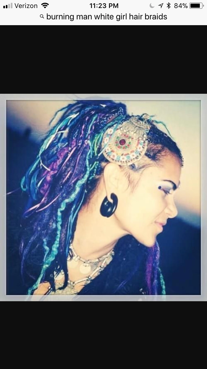 Burning Man Festival Hairstyles - Creative braided look with desert accessories A woman with intricate braids adorned with metallic beads and feathers at a dusty Burning Man campfire scene