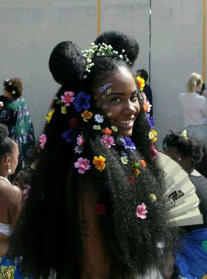 Festival hairstyle featuring intricate twists and metallic accessories for natural black hair Woman with twisted natural black hair adorned with gold cuffs and beads, smiling at a sunny festival