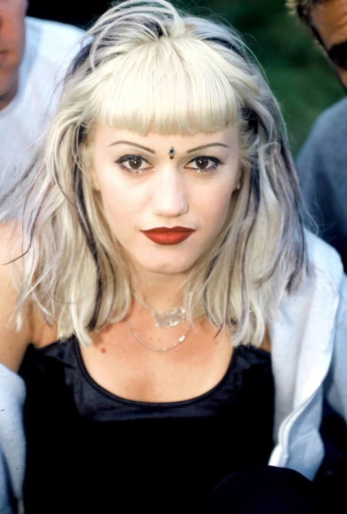 A woman with a messy grunge festival hairstyle featuring dark teased roots and platinum blonde lengths