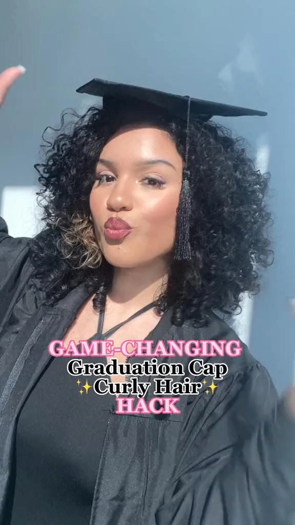 Graduating woman with natural curly hair wearing a black graduation cap and gown