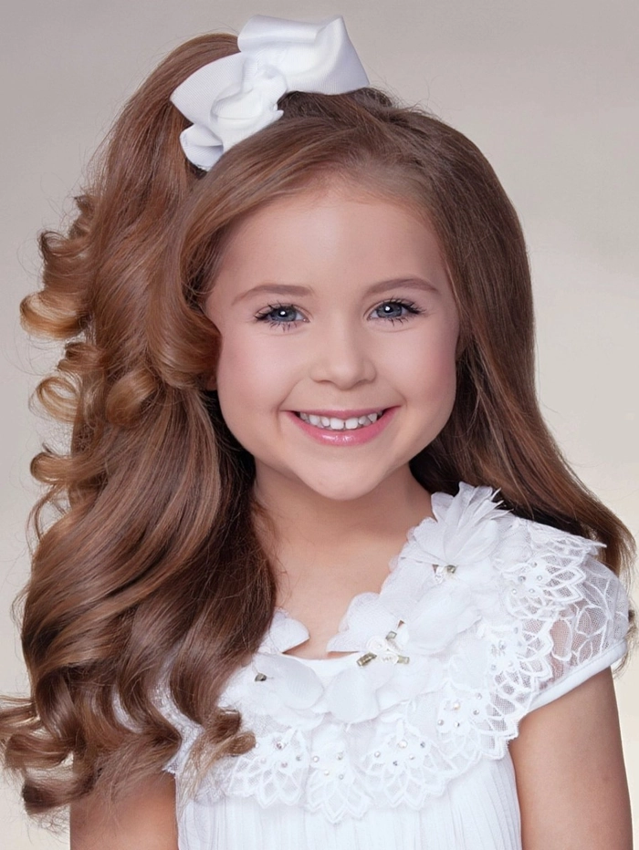 Child wearing a comfortable updo for a holiday pageant with soft curls and a sparkly bow