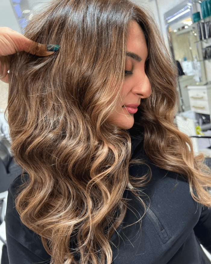 A woman with a blended summer-to-fall hair transition style featuring warm tones and soft waves
