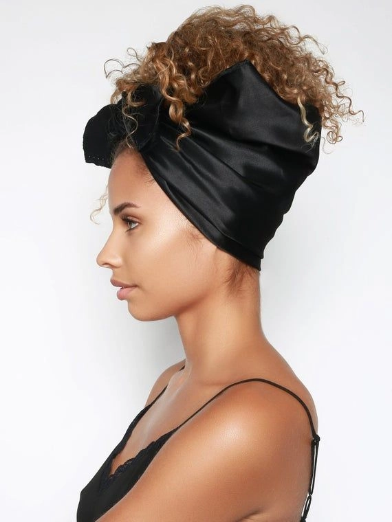 Woman wrapping a silk scarf around her head for winter hair protection, holiday hairstyle tutorial step