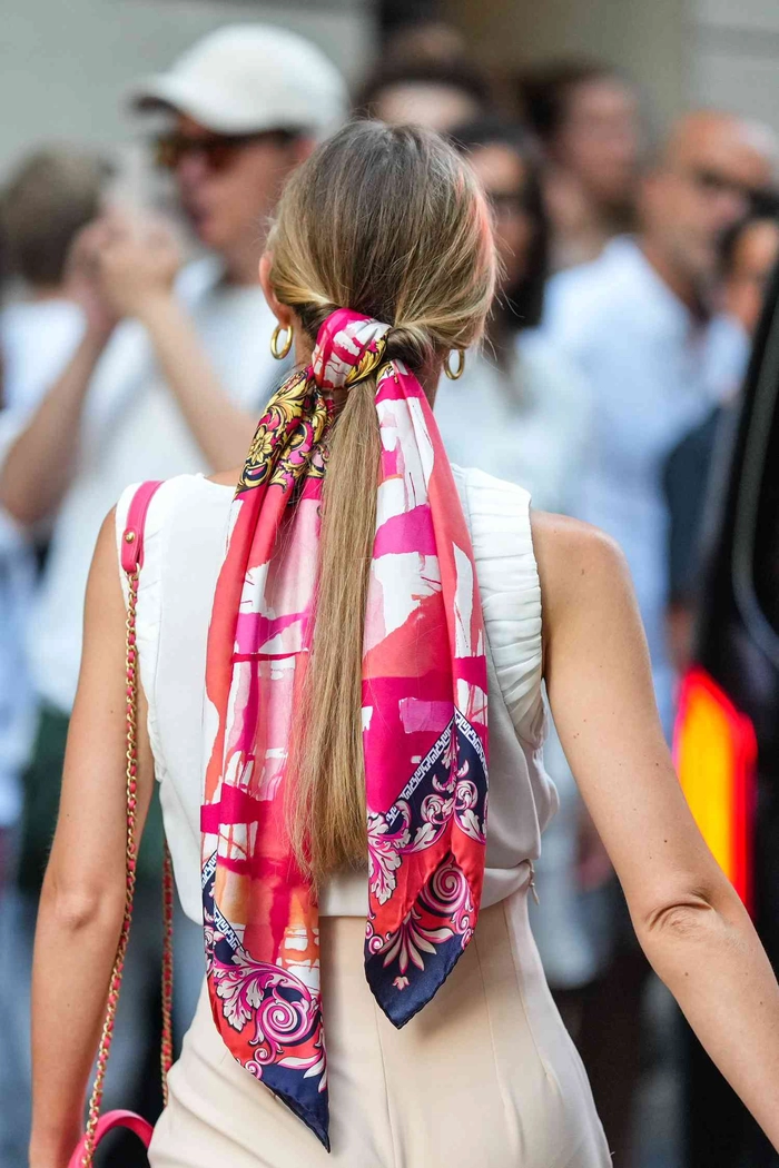 Woman wrapping a silk scarf around her hair for winter protection with festive holiday style