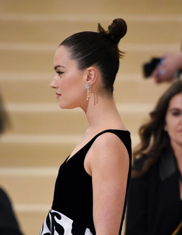 A minimalist holiday outfit features a woman with a sleek top knot bun, clean makeup, and a simple gold necklace.