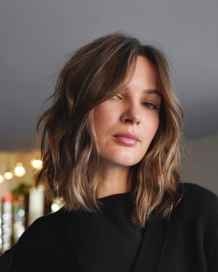 A woman wearing a textured lob hairstyle at a Friendsgiving party, with soft waves and subtle highlights
