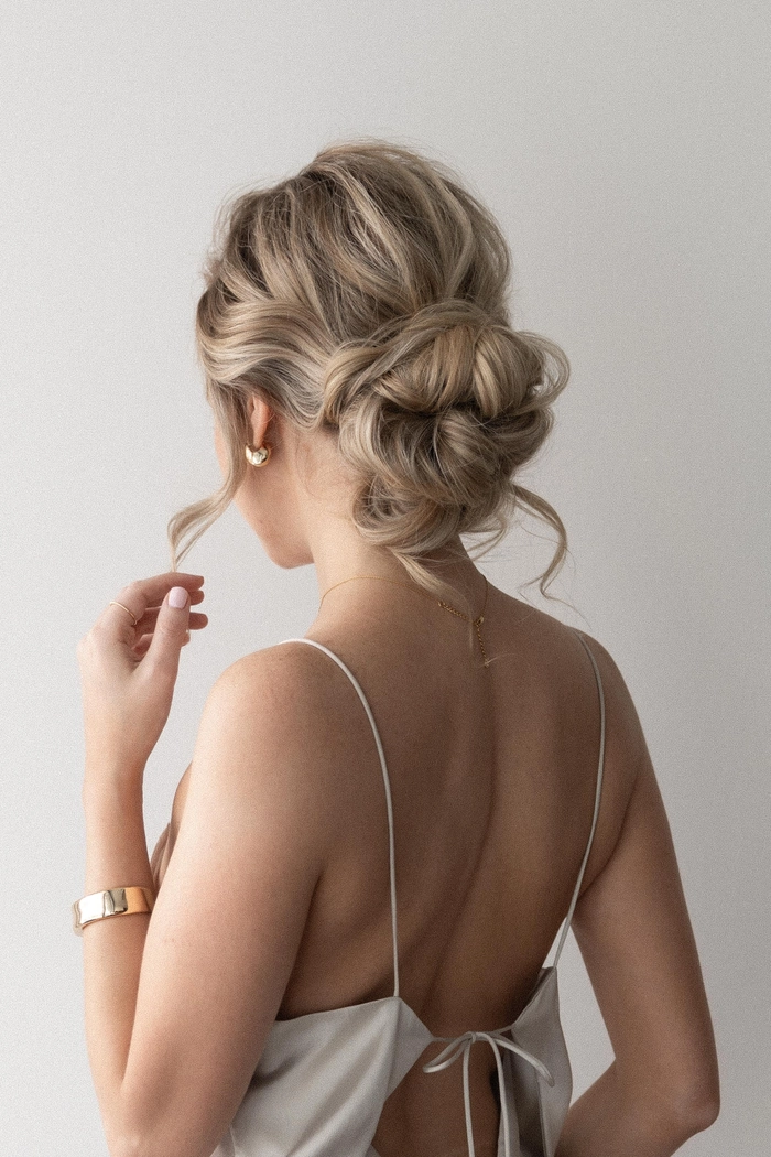 Low messy bun with face-framing pieces for a wedding guest hairstyle