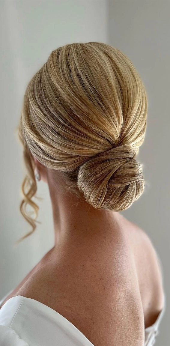Elegant low messy bun for a wedding guest with soft face framing strands