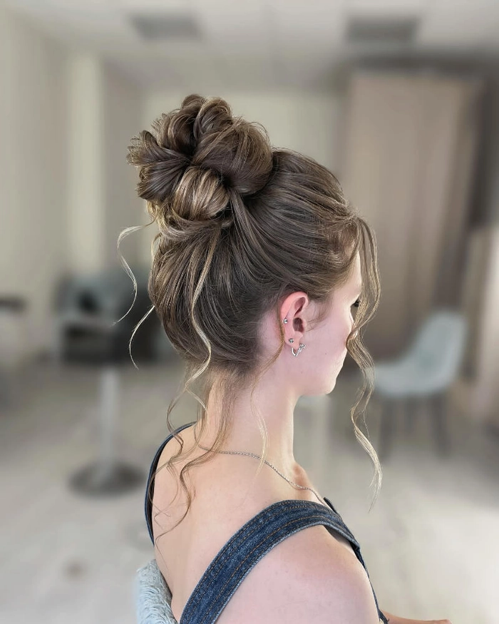Elegant prom hairstyle featuring a high messy bun with loose curls and volume