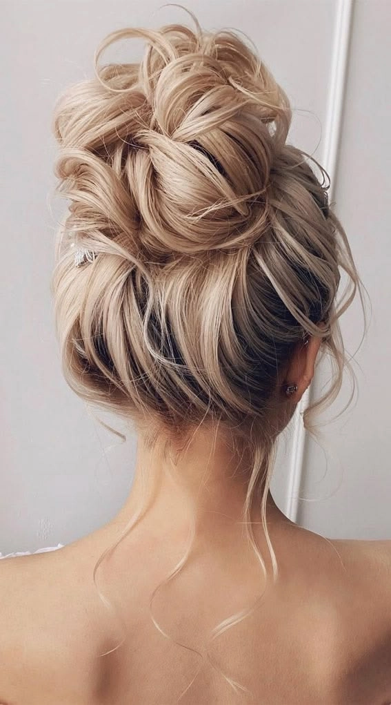 Elegant prom hairstyle featuring a high messy bun with loose strands