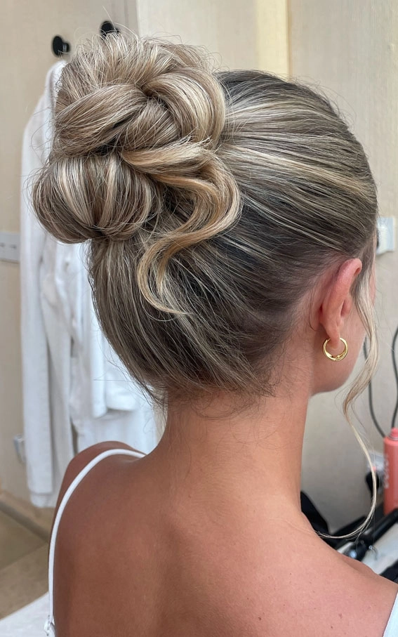Elegant prom hairstyle featuring a textured top knot with detailed braiding Textured top knot prom updo with braided accents and loose strands