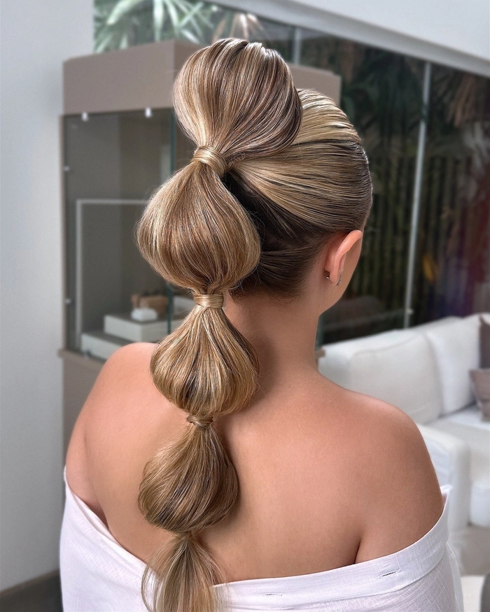 Elegant bridal hair bubble ponytail styled with soft curls and floral accents