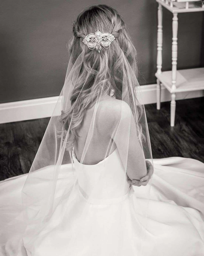 Elegant long wavy wedding hairstyle featuring a classic bridal veil Bride with long wavy wedding hair adorned with a delicate veil