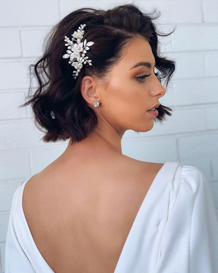 Short bob bridal hairstyle inspiration with soft waves and fresh flowers Elegant short bob wedding hairstyle featuring delicate floral accents for brides