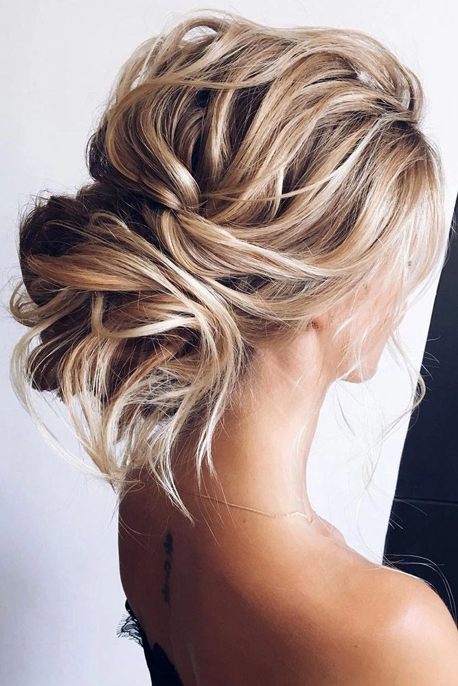 Elegant bridal hairstyle featuring a low updo with textured volume and relaxed waves Messy textured low bridal updo with loose curls and soft tendrils for a romantic wedding look