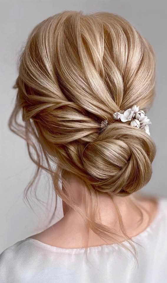 Elegant low updo with a textured, effortless bridal look for wedding day glamour Messy textured low bridal updo hairstyle featuring soft waves and delicate tendrils