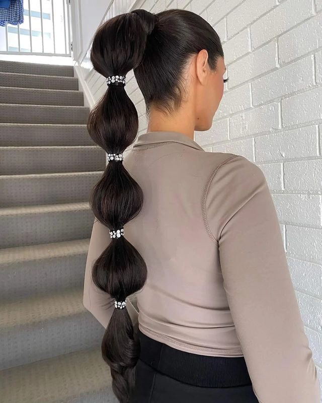 Step six of creating a bubble ponytail for the office, pulling hair sections to form distinct bubbles
