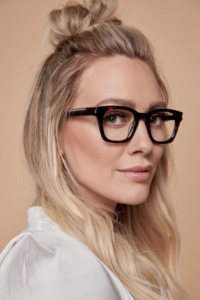 Hair tuck for glasses wearers - office style with low ponytail A woman in office attire with glasses, her hair neatly tucked behind her ears in a low ponytail
