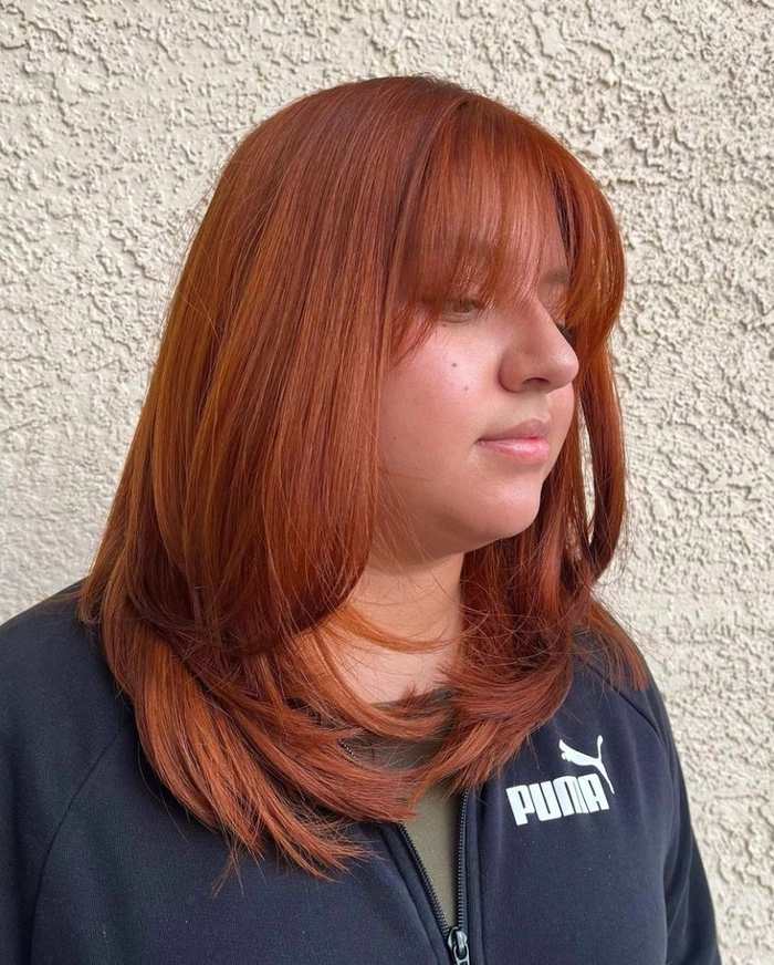 A woman with a round face shape wears face framing office layers, styled with soft waves that elongate her features