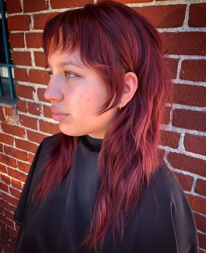 A woman with shoulder-length face-framing layers, styled to complement a round face shape, wearing professional office attire.