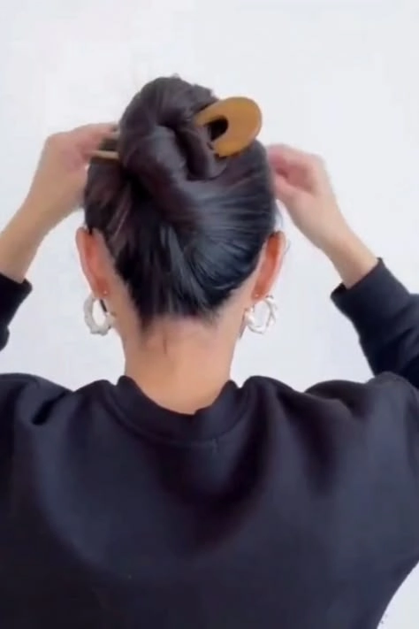 Sleek low office bun secured with two minimalist hairpins against a neutral background